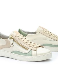 Baskets à lacets en cuir beige et vert menthe avec une semelle blanche texturée, dotées d'un détail zippé sur le côté et d'accents contrastants.