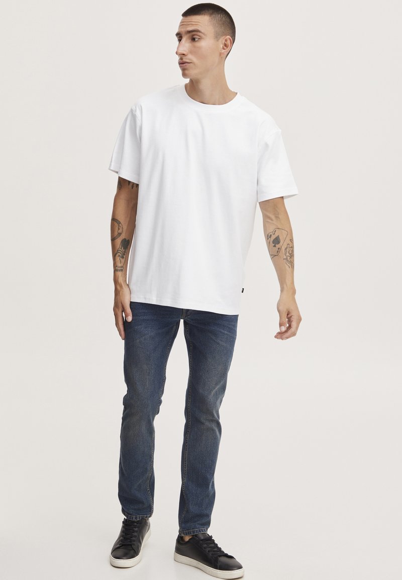 Witte katoenen t-shirt met korte mouwen, ronde hals, en een relaxte pasvorm. Gecombineerd met donkerblauwe jeans en zwarte sneakers.