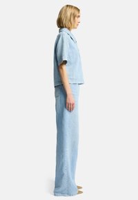 Lys blå denimoutfit bestående af en kortærmet top og højtaljede, vide bukser, der viser en afslappet pasform og minimalistisk design.