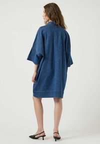 Vestido estilo kimono de denim en azul profundo, con mangas amplias, de longitud media y un corte relajado. Textura de tela natural visible. Detalle de costura sutil.