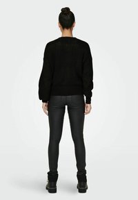 Czarny sweter z grubym splotem i opuszczonymi ramionami, zestawiony z czarnymi dopasowanymi spodniami i masywnymi czarnymi butami, prezentujący teksturowany wzór dzianiny.