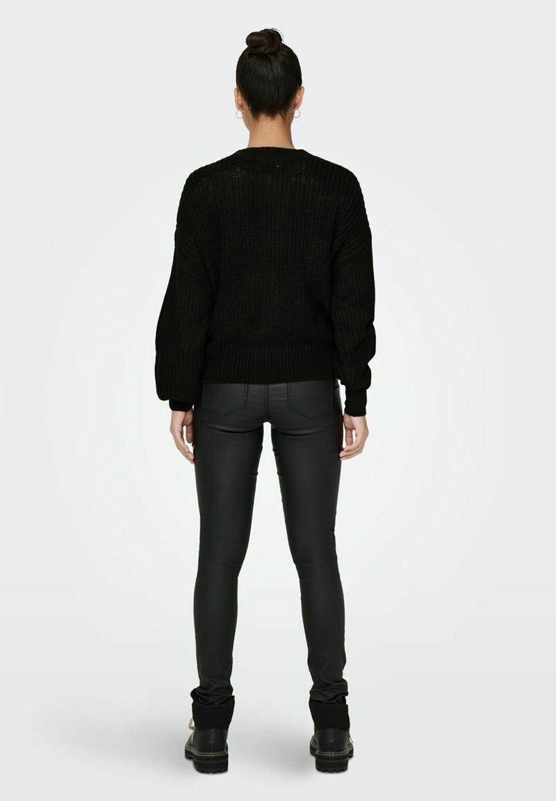 Czarny sweter z grubym splotem i opuszczonymi ramionami, zestawiony z czarnymi dopasowanymi spodniami i masywnymi czarnymi butami, prezentujący teksturowany wzór dzianiny.