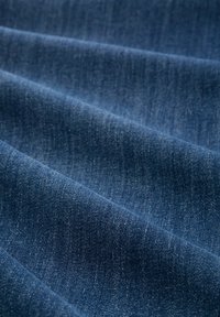 Denimová tkanina v tmavomodrej farbe s jemnou textúrou, s jemnými variáciami farby a hladkým, mierne lesklým povrchom.
