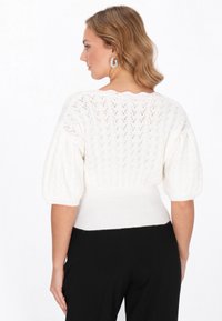 Fehér kötött pulóver, texturált cikk-cakk mintával, ballon ujjakkal és bordás aljúval. Finom fonal részletek jellemzik.