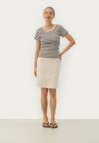 T-shirt ajusté rayé marron et blanc avec un col rond associé à une jupe beige, complété par des tongs marron.