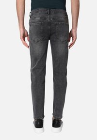 Jeans in denim grigio scuro con vestibilità slim, cinque tasche e una finitura leggermente sbiadita. Indossati con sneakers nere.