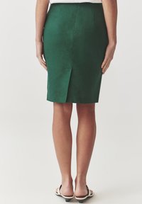 Pantaloni fustă din in verde, cu slit la spate, până la genunchi. Textură netedă, design ajustat și siluetă simplă. Încălțăminte casual vizibilă.