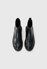 Black leather ankle boots with broguing details, round toes, elastic side panels, and textured black rubber soles.