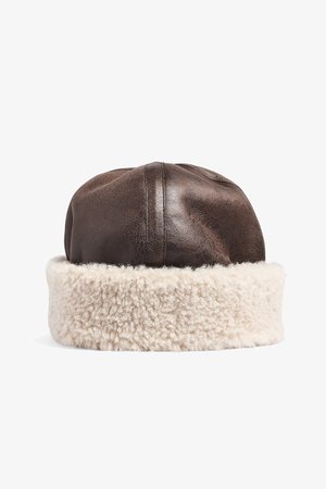 Brown leather cap with a plush cream faux shearling band. Rounded top with visible stitching. Soft texture throughout.