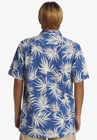 Camisa de manga corta, azul, con un patrón de hojas de palma en blanco y coral, fabricada en tela ligera, con cuello puntiagudo y corte relajado.