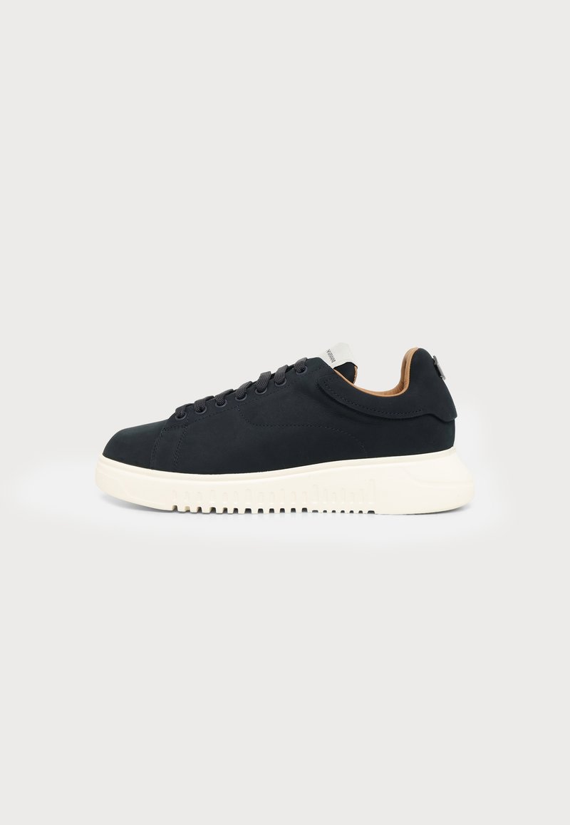 Baskets noires à lacets avec une semelle blanche épaisse et une doublure beige, vues de profil sur un fond clair uni.