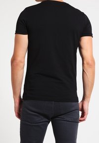 Czarny t-shirt z krótkim rękawem, charakteryzujący się okrągłym dekoltem, gładką tkaniną i dopasowanym krojem. Noszony z ciemnoszarymi spodniami.
