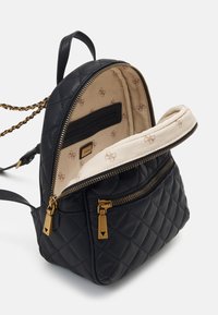 Mochila de cuero negro acolchada con herrajes dorados, que cuenta con un bolsillo interior con cremallera y un forro beige con un patrón de logo repetido.