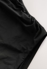 Crne kupaće gaće izrađene od glatkog, laganog materijala. Imaju nabranu detalj na struku i kontrastni teksturirani rub.