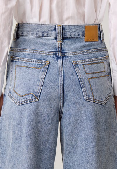 Jeans in denim azzurro chiaro con vita alta, gambe dritte e tasche posteriori pronunciate. Presentano un'etichetta in finta pelle color cuoio e cuciture gialle.