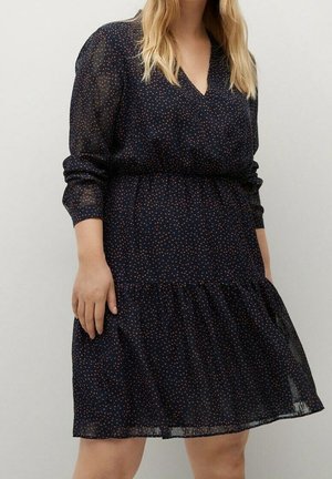 Femme portant une robe noire à manches longues avec de petits pois multicolores, col en V, taille froncée et jupe évasée.