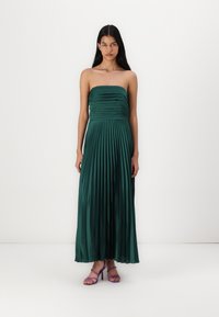 Strapless zeleni nabrani maxi haljina od satenskog materijala, s uskim gornjim dijelom i lepršavom suknjom, uparen s ljubičastim sandalama s trakicama.