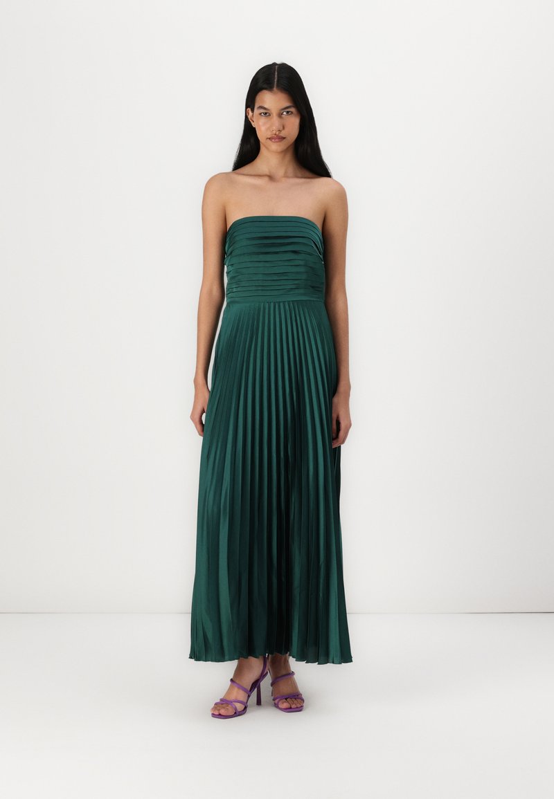 Strapless zeleni nabrani maxi haljina od satenskog materijala, s uskim gornjim dijelom i lepršavom suknjom, uparen s ljubičastim sandalama s trakicama.