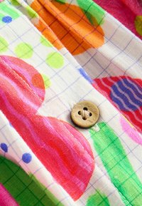 Tissu en coton coloré présentant de grands cercles et des rayures en rose, orange, vert et bleu, avec un bouton marron accentuant le design.
