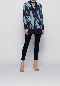 Blå och marinblå cardigan med tigermönster, som har v-ringning, stora framknappar och sidofickor, i kombination med mörka slim fit byxor.