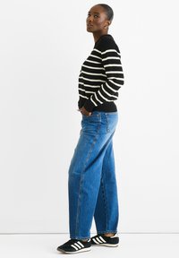 Black and white striped sweater with ribbed cuffs, paired with high-waisted blue denim jeans and black sneakers with white stripes.