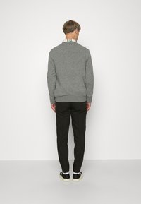 Grå stickad tröja med rund halsringning, bärs med svarta byxor och svarta sneakers, sedd bakifrån. Enkel, samtida design.