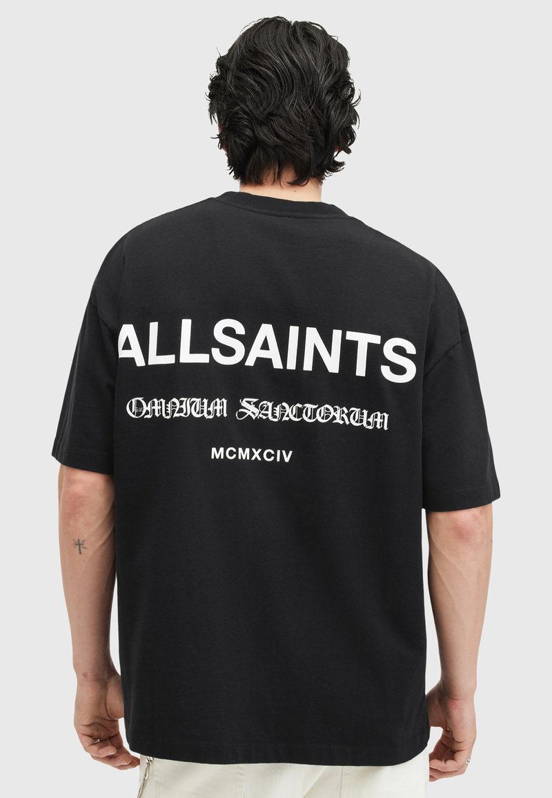 Melnas kokvilnas t-krekls ar izteiksmīgu baltu tekstu "ALLSAINTS" un sarežģītu rakstu uz muguras. Īsas piedurknes un brīvs griezums.