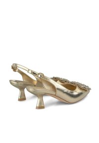 Zapatos slingback metálicos dorados con un tacón bajo y acampanado y un borde decorado en la parte frontal. Textura suave con un acabado brillante.