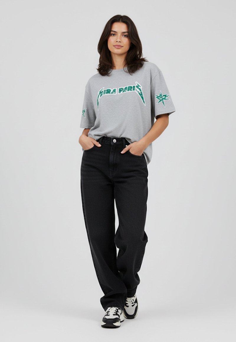 Grijze oversized t-shirt met groene grafische tekst "HERA PARIS," gecombineerd met hoge zwarte jeans en zwart-witte sneakers.