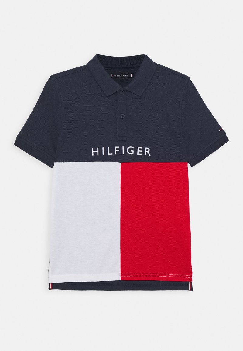 Polo bleu marine avec empiècements blancs et rouges, manches courtes, patte à deux boutons, et texte "HILFIGER" sur la poitrine.