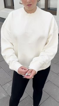 Sweatshirt oversize branco com punhos e decote canelados, apresentando uma discreta marcação em relevo. Combinado com leggings pretas.