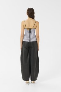 Camisole in satin grigio con spalline nere sottili, caratterizzato da un dettaglio nella parte posteriore con nodo. Abbinato a pantaloni in pelle nera a vita alta.