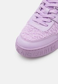 Lila sneakers med en texturerad, fluffig ovandel och läderdetaljer, samt präglad logotyp på gummisulan. Snörena är färgmatchade.