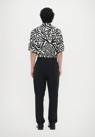Short-sleeve shirt in white with black abstract patterns, paired with black tapered pants, featuring an elastic waistband and minimal hardware.