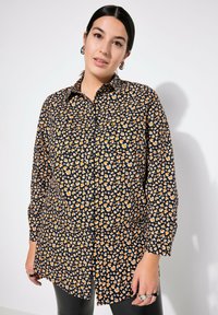 Zwarte shirt met een oranje en witte hartpatroon, knoopsluiting, lange mouwen en een standaard kraag, gemaakt van een lichte stof.
