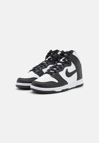 Zapatillas altas en blanco y negro con material de cuero, puntera perforada, cordones redondos y suela de goma contrastante con dibujo antideslizante.