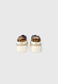Paire de baskets blanches à plateforme avec détails imprimé léopard et logo "Buffalo" sur le talon sur fond gris uni.