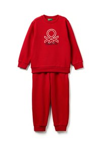 Červená souprava mikiny a kalhot s žebrovanými manžetami, na přední straně mikiny uprostřed je bílo-černé logo Benetton.