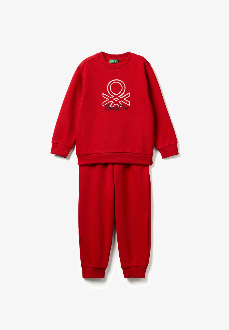 Červená souprava mikiny a kalhot s žebrovanými manžetami, na přední straně mikiny uprostřed je bílo-černé logo Benetton.