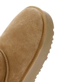 Tan suède enkellaars met een ronde neus, gestructureerd oppervlak en rubberen zool met een profielpatroon voor grip. Decoratieve stiksels op de naad.