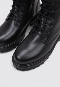 Bottes de cheville en cuir noir avec une surface lisse, bout rond, design à lacets, et semelle en caoutchouc épaisse pour durabilité et traction.