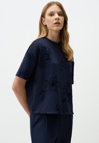 Navyblauw oversized t-shirt met korte mouwen, voorzien van een geperst bloempatroon en een ronde halslijn. Zacht, textuurstof.