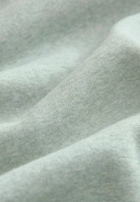 Lichtgroene katoenen stof met een zachte, gestructureerde oppervlakte, met zachte plooien en subtiele variaties in de tint.