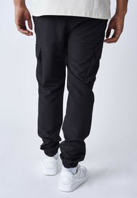Pantalones cargo negros con bolsillos laterales, puños elásticos y un corte relajado, combinados con zapatillas blancas y calcetines grises.