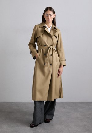 Beige trenchcoat med bælte i taljen, dobbeltradet knaplukning, brede revers og lange ærmer. Sammen med grå vide bukser.