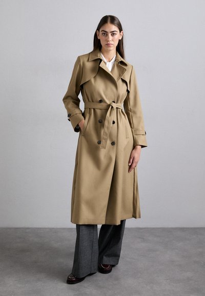 Beige trenchcoat med bælte i taljen, dobbeltradet knaplukning, brede revers og lange ærmer. Sammen med grå vide bukser.
