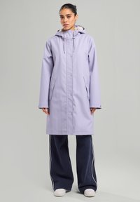 Light lavender waterproof coat with a hood, featuring snap buttons, side pockets, and a soft inner lining. Paired with navy wide-leg pants.