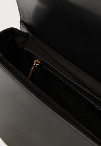 Melns ādas rokassomiņa ar gludu ārpusi un auduma oderi, kurai ir zelta rāvējslēdzējs un iekšējais kabats organizācijai.