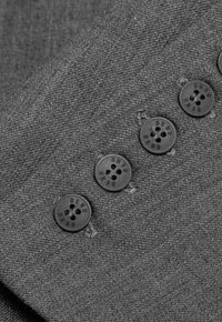 Szary materiał z subtelną teksturą, na którym znajdują się sześć czarnych guzików z czterema otworami. Każdy guzik ma wyraźne grawery. Ułożone pod kątem.