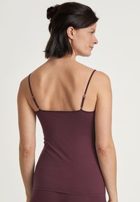 Bordeaux tanktop met smalle verstelbare bandjes en een getailleerd ontwerp, gemaakt van gladde, rekbare stof. De achterkant toont een rechte snit.
